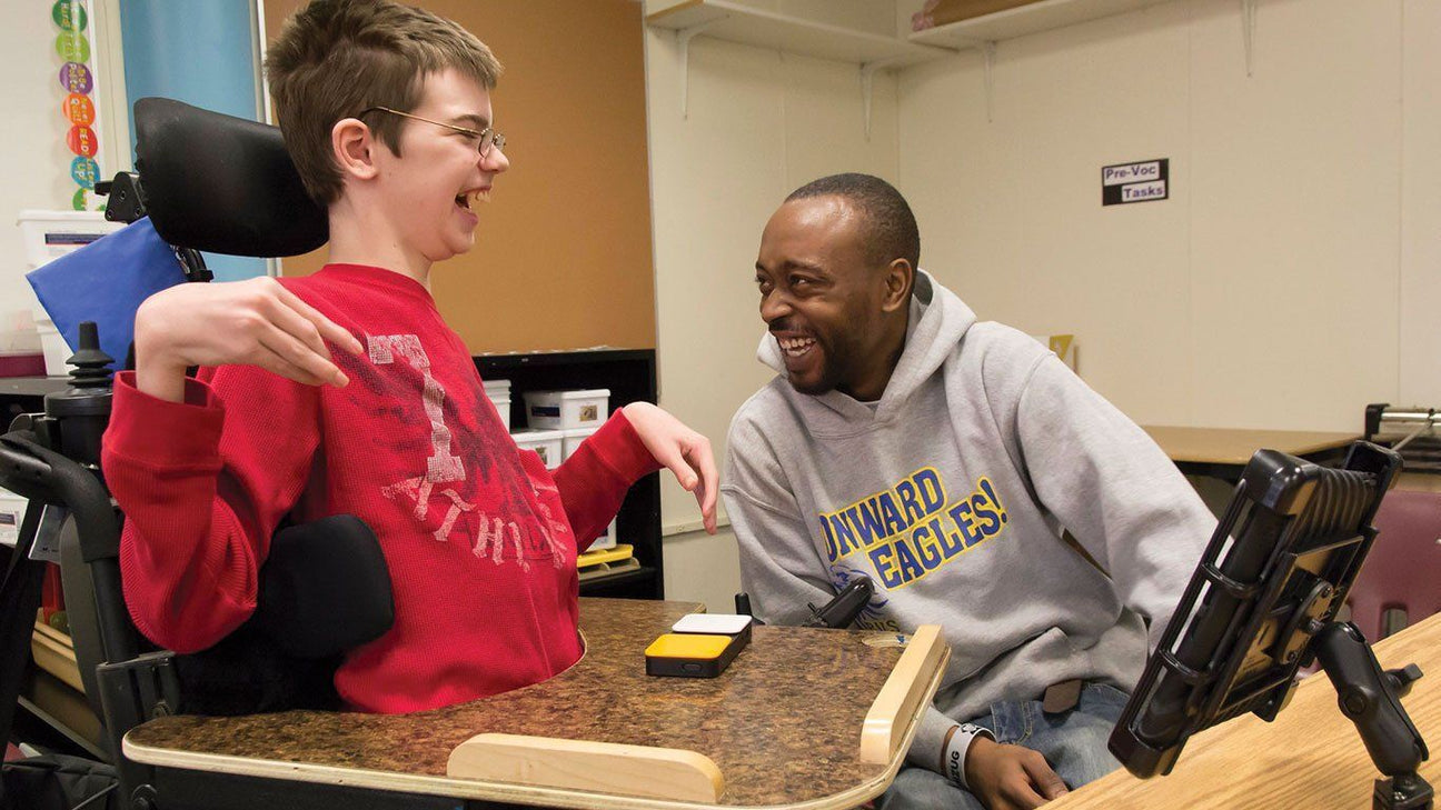 A learner useing a scanning keyboard working with an educator and laughing.